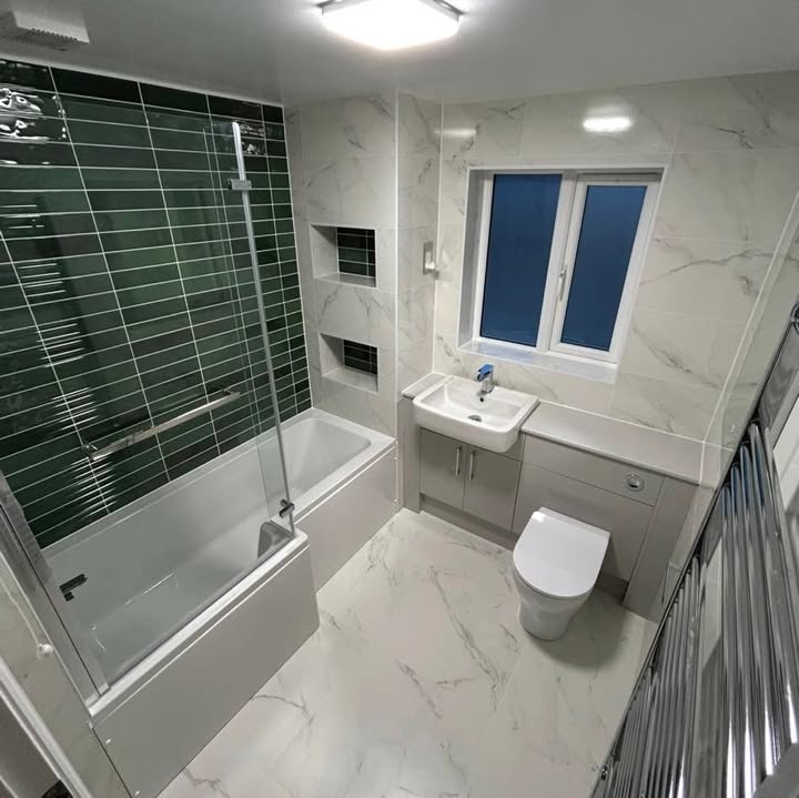 Bathroom with green metro tiles, marble-effect walls and floor and a bath with glass screen
