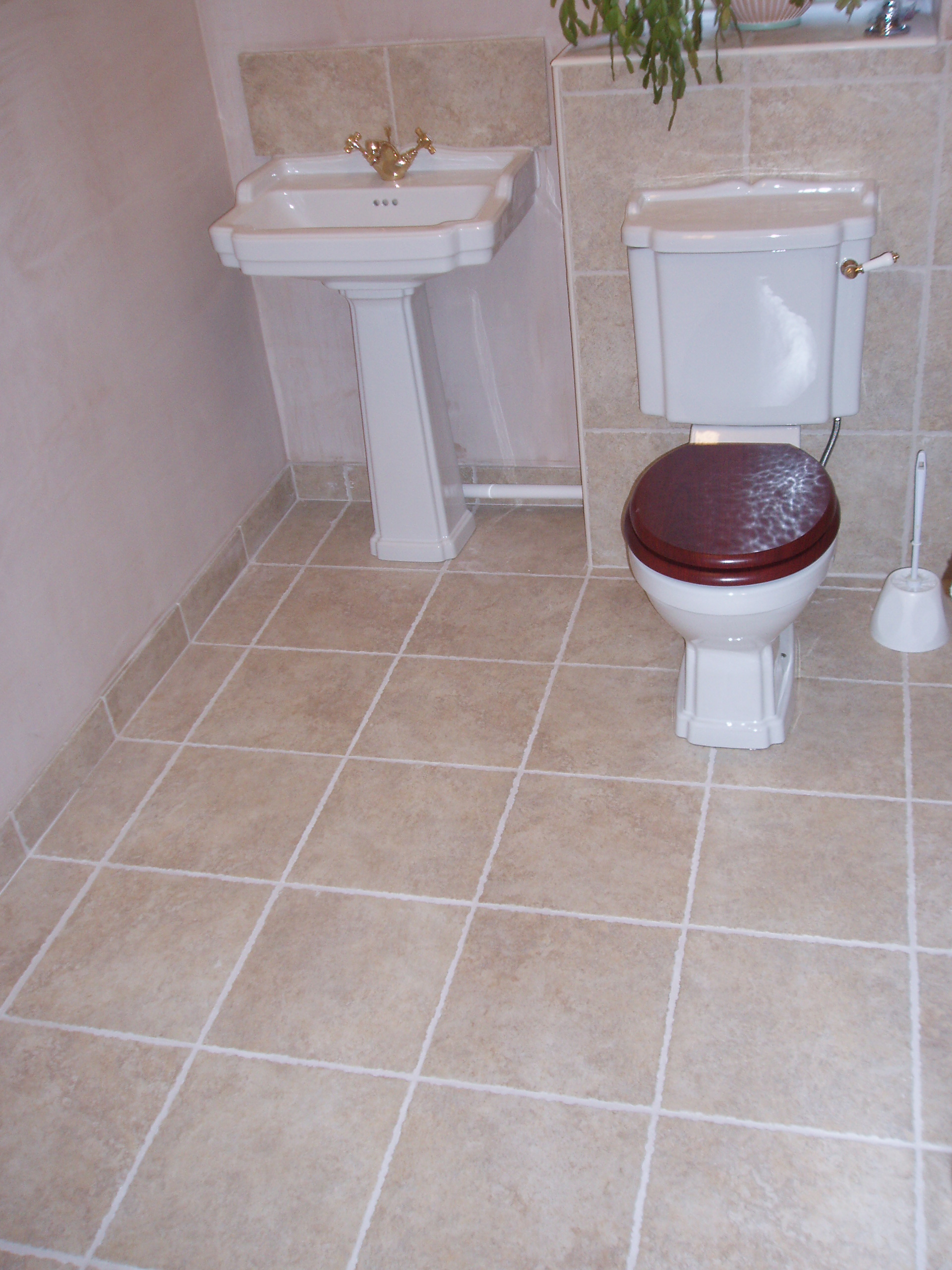 Traditional pedestal basin and close-coupled toilet with gold taps on a stone floor