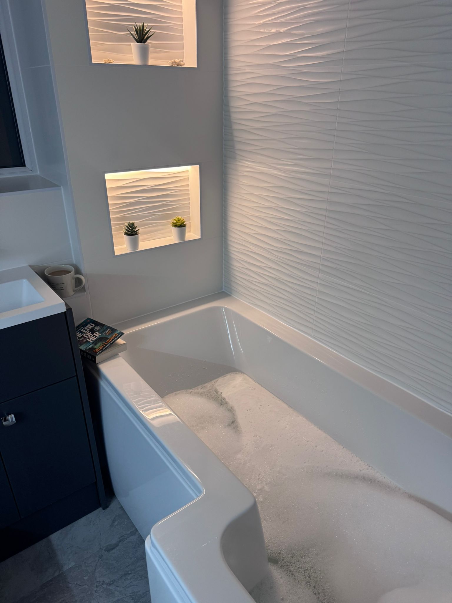 P-shaped bath with white wave wall tiles and lit shelving niches