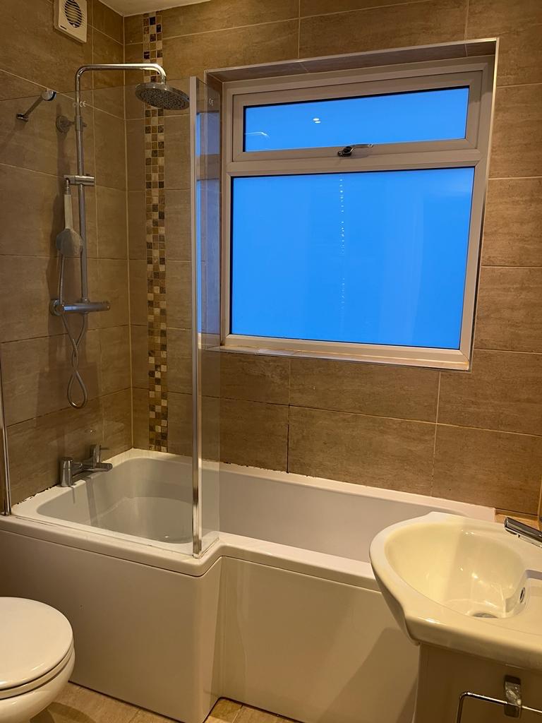 L-shaped shower bath under a window with warm stone-effect tiles