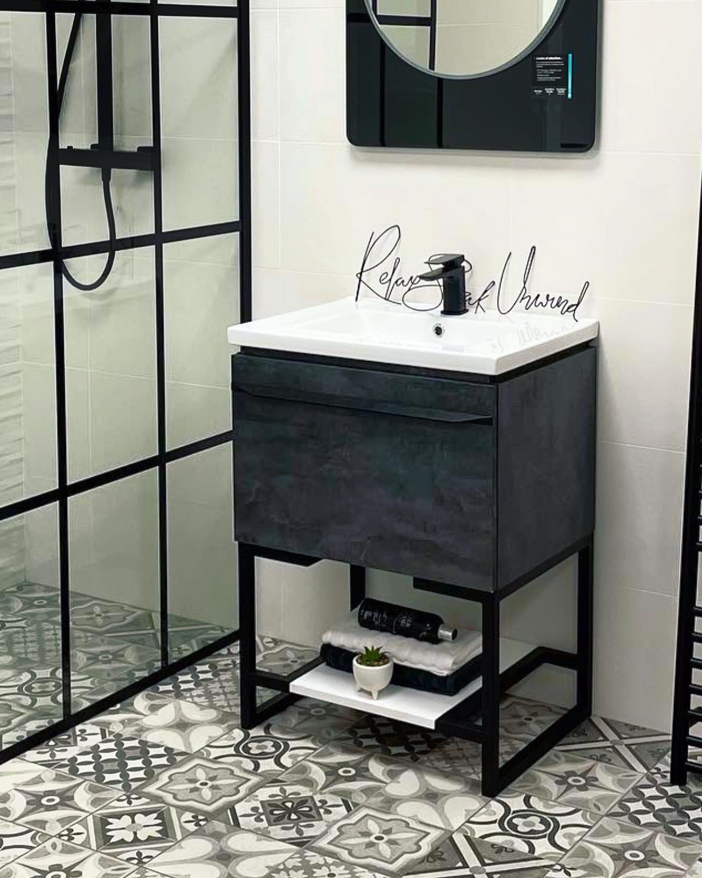 Showroom display with a black-framed shower screen and charcoal vanity on a patterned floor